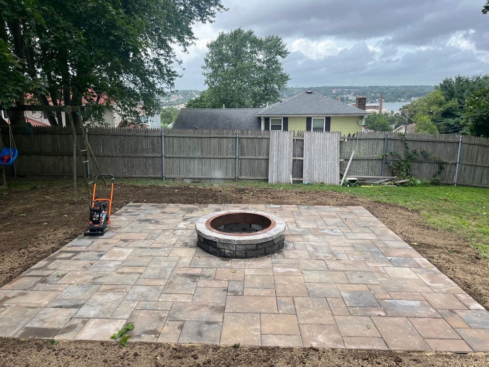 Patio area with a stone fire pit and landscaping tools in a residential backyard.