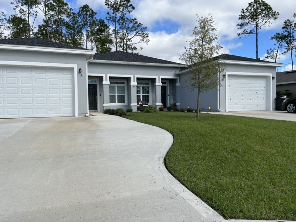 Modern single-story home with two garages and manicured lawn under a blue sky.